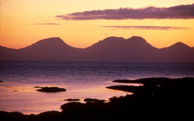 LOOKING ACROSS TO THE DISTINCTIVE OUTLINE OF THE PAPS OF JURA (THREE HIGHEST PEAKS OF THE ISLAND, BEINN AN OIR, BEINN SHIANTAIDH AND BEINN A' CHAOL) ON THE ISLE OF JURA, AT SUNSET, INNER HEBRIDES